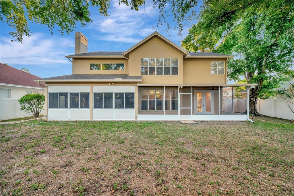 The rear exterior of a two-story house features a large screened-in porch and lawn — 2839 SAFE HARBOR DRIVE, TAMPA, FL