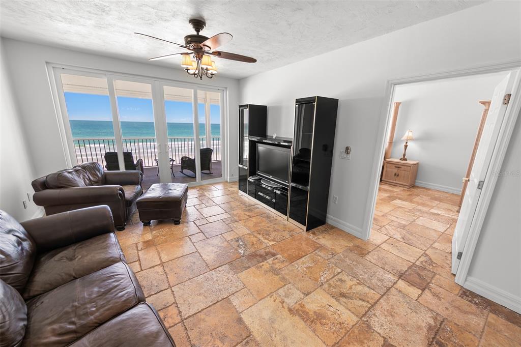 A living room with tile flooring, leather furniture, a media center, and a balcony overlooking water — 4767 S ATLANTIC AVENUE UNIT 402, PONCE INLET, FL