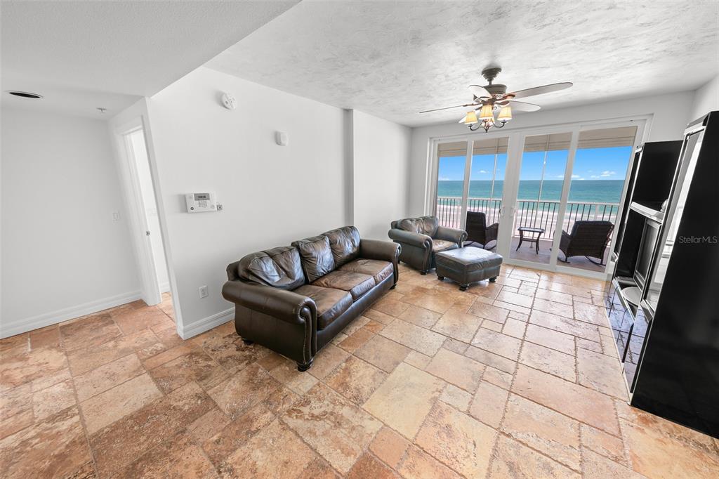 A living room with tile flooring, leather furniture, and a balcony overlooking the ocean — 4767 S ATLANTIC AVENUE UNIT 402, PONCE INLET, FL