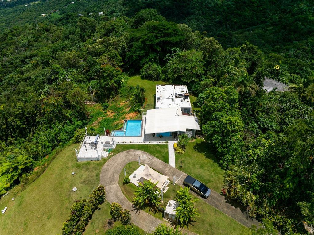 An aerial view shows a modern house with a swimming pool nestled in a lush forest — PR 797 km 5.3 JAGUEYES WARD, AGUAS BUENAS, PR