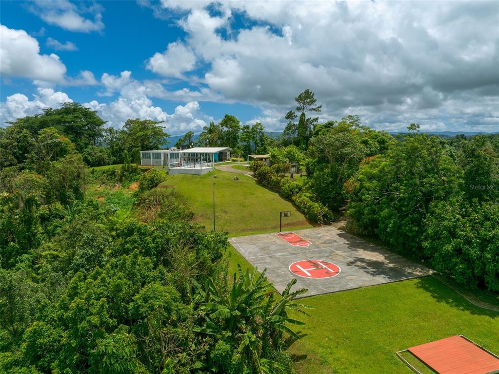 An aerial view shows a house with a basketball court and helipad on a grassy hill — PR 797 km 5.3 JAGUEYES WARD, AGUAS BUENAS, PR