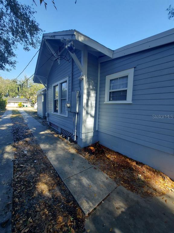 A side view of a blue house with horizontal siding, a concrete walkway, and exposed rafters — 616 W HOWRY AVENUE, DELAND, FL