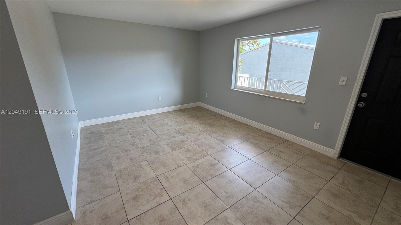 An empty room features light gray walls, beige tile flooring, and a window with exterior views — 1955 NW 5th Pl # 11, Miami FL 33136, MIAMI, FL