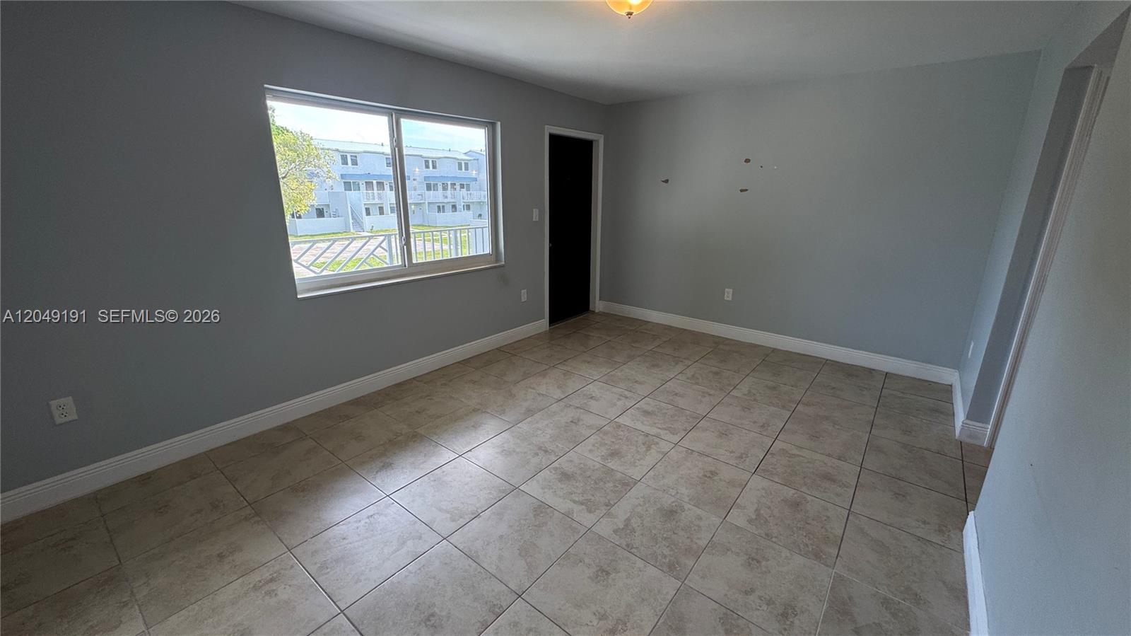 An empty room features light gray walls, large beige floor tiles, and a sliding window — 1955 NW 5th Pl # 11, Miami FL 33136, MIAMI, FL