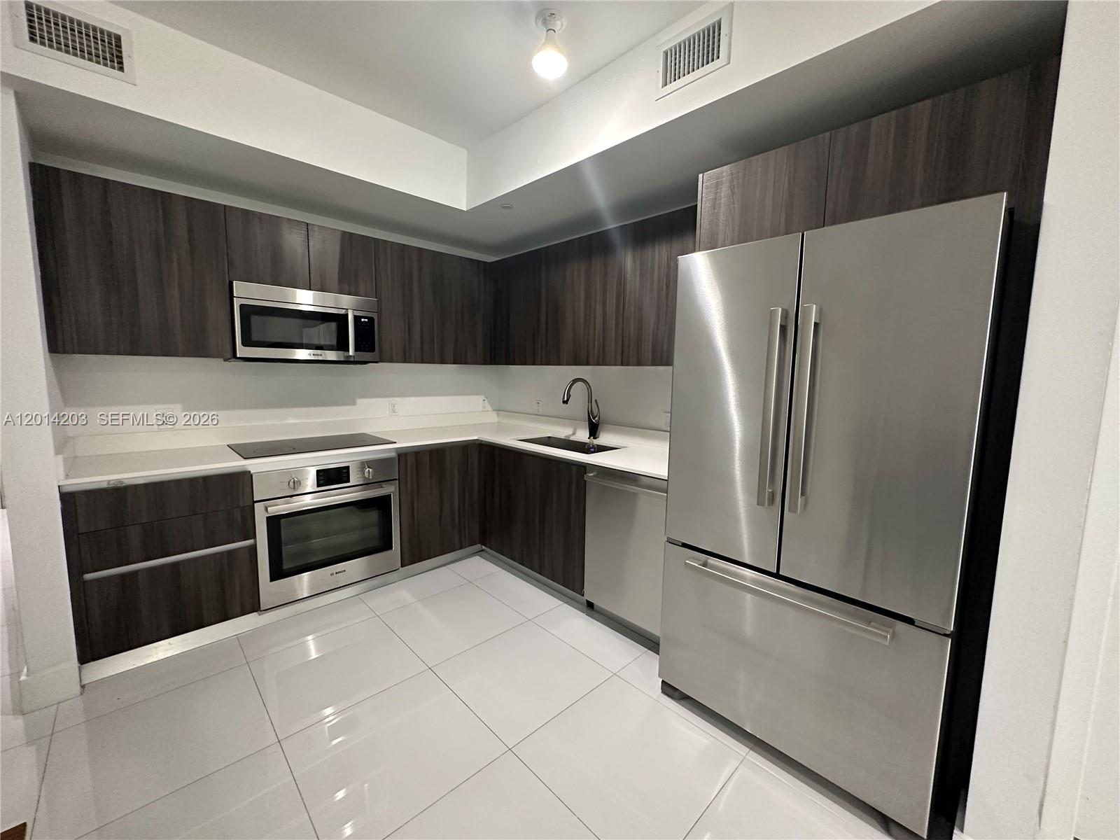 A modern kitchen features dark wood cabinets, stainless steel appliances, and white tile flooring — 488 NE 18th St # 2502, Miami FL 33132, MIAMI, FL