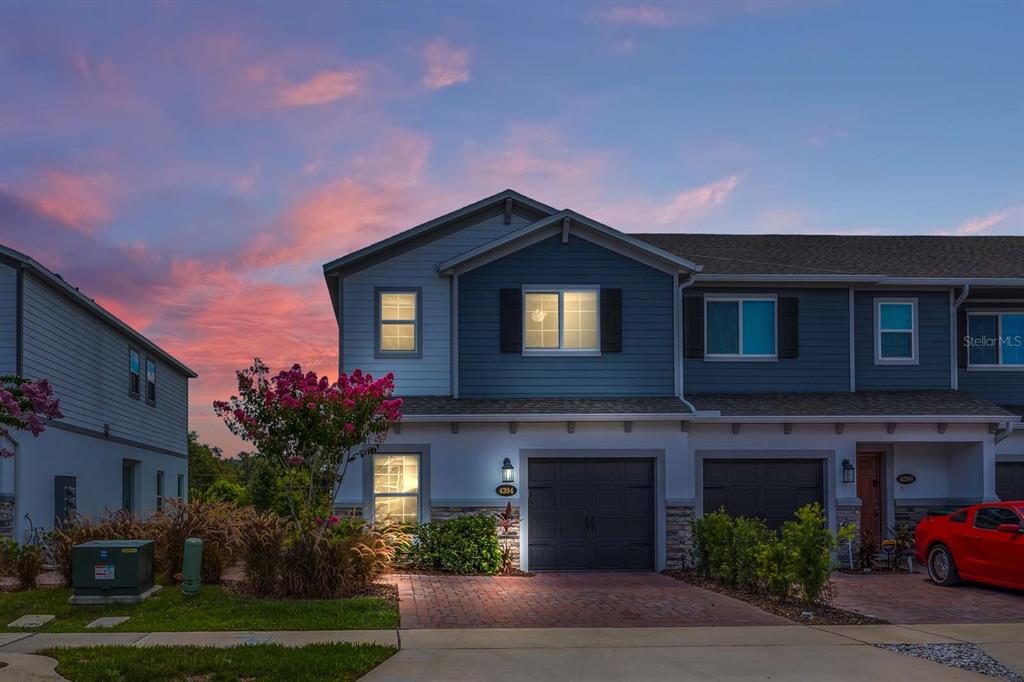 A two-story townhouse with blue siding, a brick driveway, and a garage at sunset — 4394 CAMPSITE LOOP, ORLANDO, FL