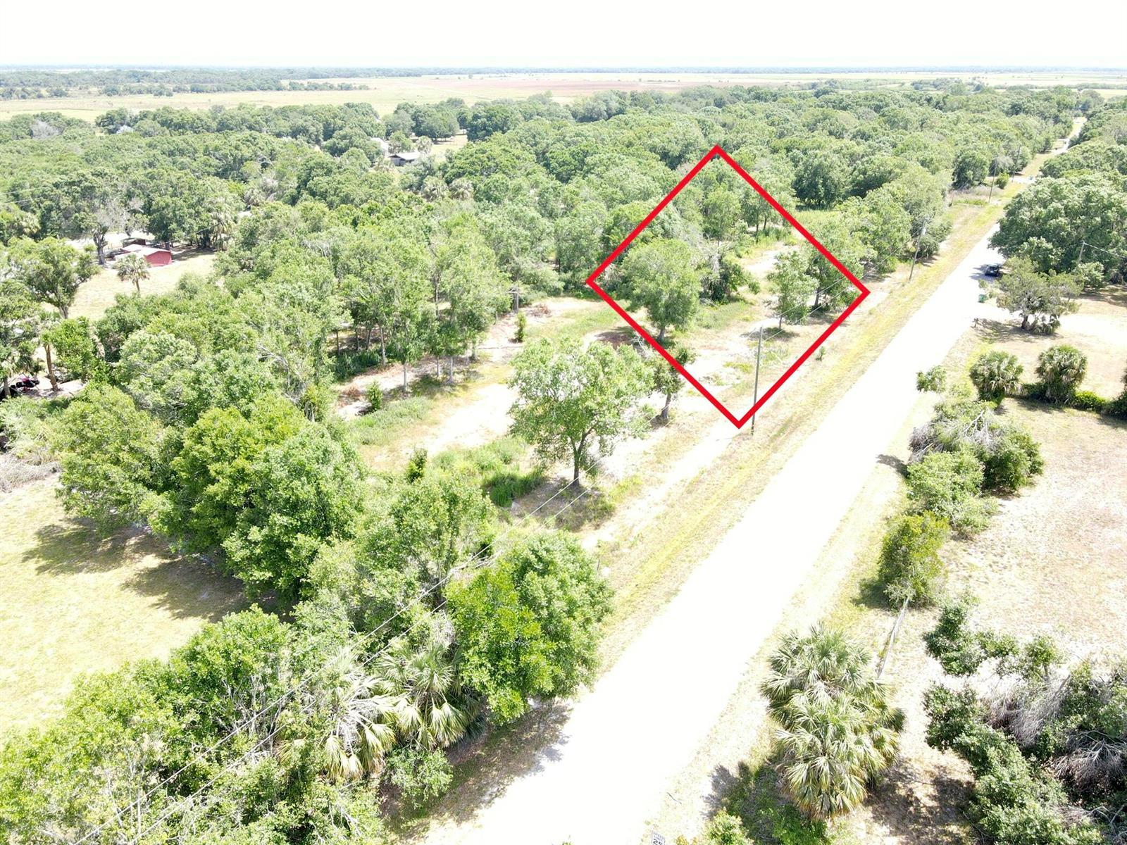 An aerial view shows a vacant, tree-covered lot outlined in red next to a road — 7771 NW 93rd Court, Okeechobee FL 34972, OKEECHOBEE, FL