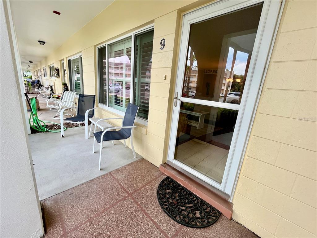 A covered patio features a glass storm door, outdoor seating, and a green garden hose — 2223 PHILIPPINE DRIVE UNIT 9, CLEARWATER, FL