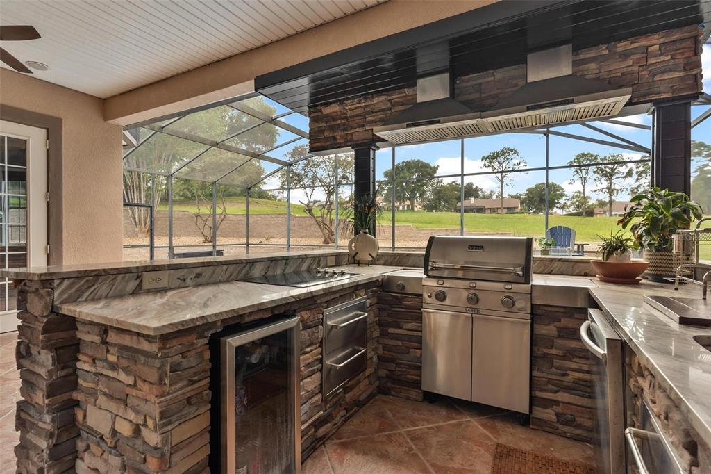 An outdoor kitchen features stone veneer, granite countertops, stainless steel appliances, and a screened-in view — 5506 CITATION COURT, LADY LAKE, FL