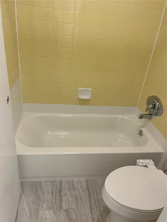 A bathroom features a white bathtub with yellow tiled walls and a white toilet — 234 KRIDER ROAD, SANFORD, FL