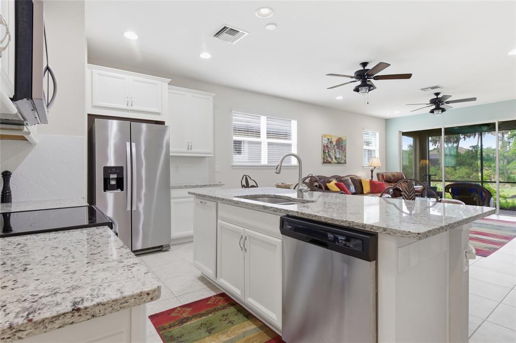 A kitchen with white cabinets, granite countertops, and stainless steel appliances overlooks a living area — 11940 TAPESTRY LANE, VENICE, FL