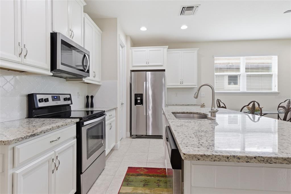 A kitchen features white cabinets, granite countertops, stainless steel appliances, and a central island — 11940 TAPESTRY LANE, VENICE, FL