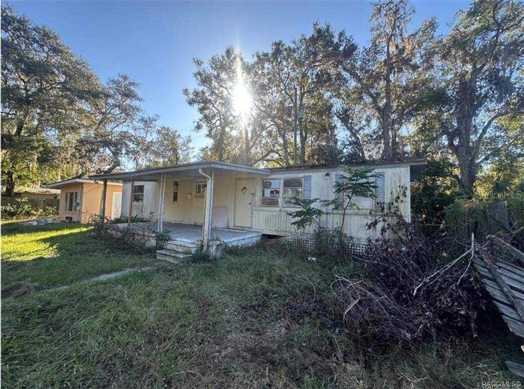 A single-story mobile home with a front porch sits on a grassy, overgrown lot — 8832 E FREEMAN COURT, FLORAL CITY, FL