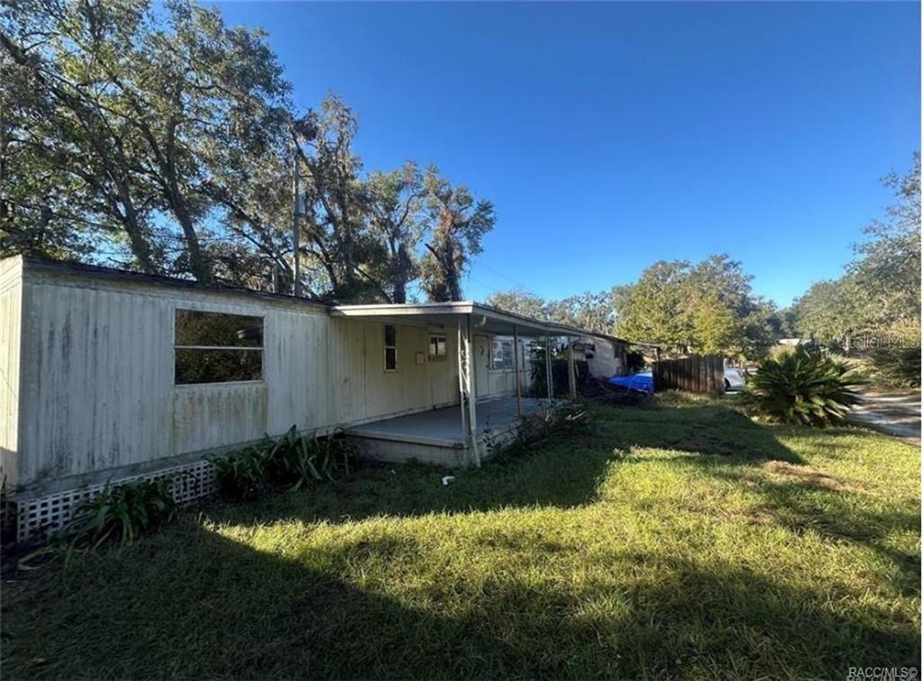 A weathered mobile home with a covered front porch sits on a grassy lot — 8832 E FREEMAN COURT, FLORAL CITY, FL