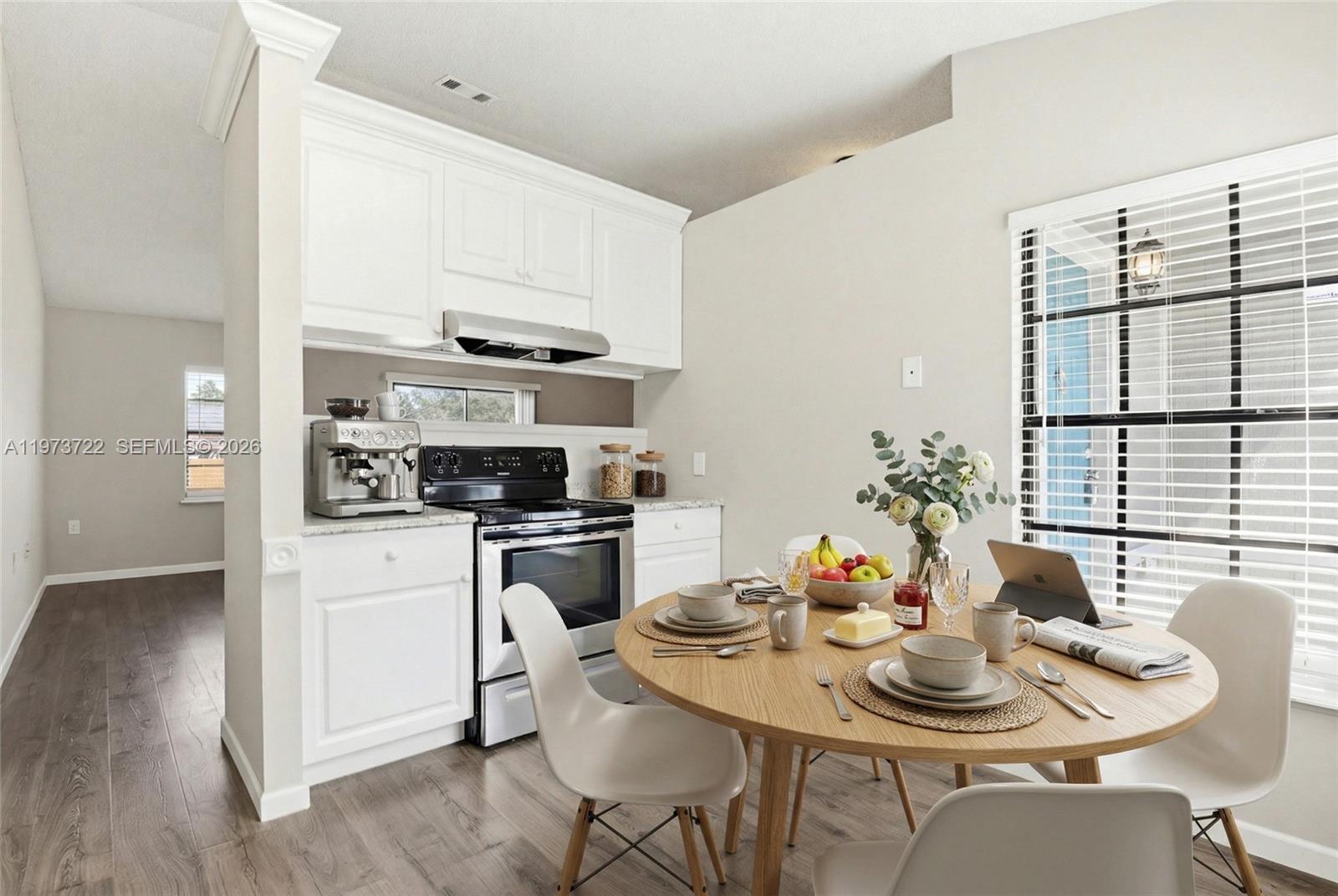 A kitchen with white cabinets and a round wooden dining table sits beside a window — 637 Mosquero Ave, Deltona FL 32738, DELTONA, FL