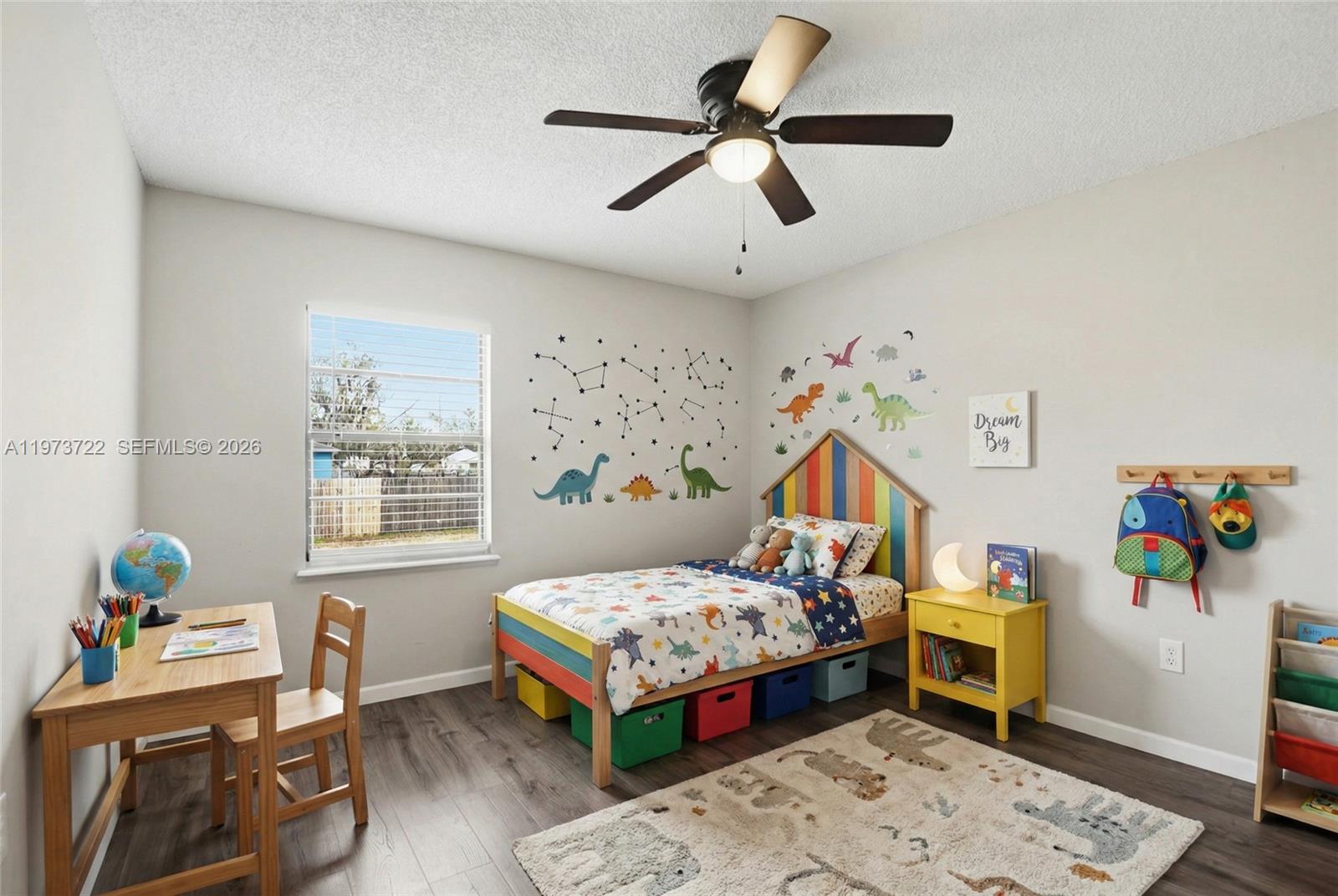 A child's bedroom features a dinosaur-themed bed, colorful storage bins, a desk, and wood flooring — 637 Mosquero Ave, Deltona FL 32738, DELTONA, FL