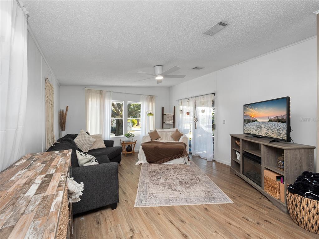 A living room features light wood flooring, a dark sofa, a television console, and white walls — 216 ELLSWORTH DRIVE, KISSIMMEE, FL