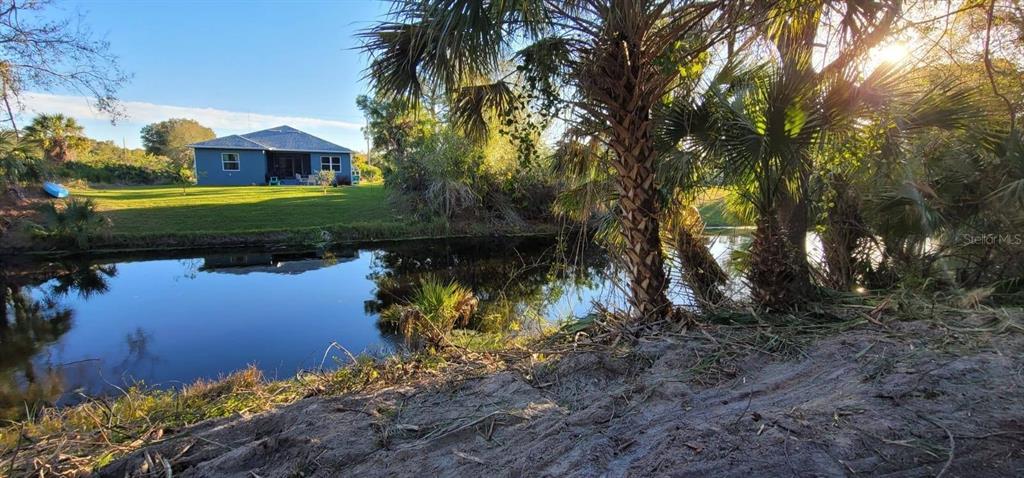 A blue house sits across a canal with palm trees in the foreground — 12395 SUNNILAND AVENUE, PORT CHARLOTTE, FL