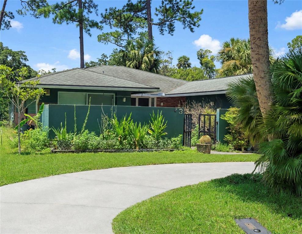 A single-story house with a green privacy wall, a concrete driveway, and surrounding palm trees — 3 CROMPTON PLACE, PALM COAST, FL
