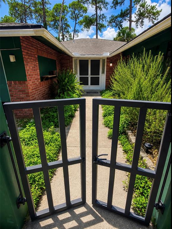 A concrete walkway leads through an open metal gate toward the front entrance of a house — 3 CROMPTON PLACE, PALM COAST, FL