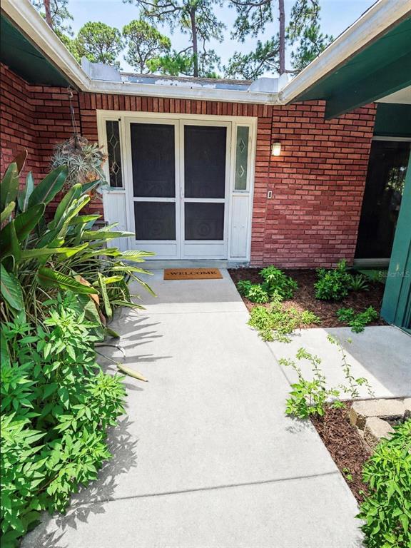 A concrete walkway leads to a double-door entrance with a screen door and brick exterior — 3 CROMPTON PLACE, PALM COAST, FL