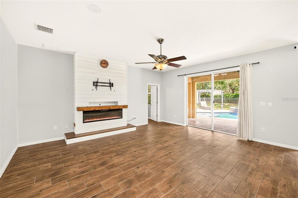A living room features wood-look tile floors, a white shiplap fireplace, and sliding glass doors — 2917 WINGLEWOOD CIRCLE, LUTZ, FL