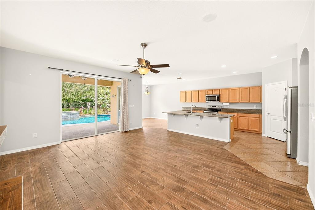 An open-concept living area features wood-look tile flooring, a kitchen with wooden cabinets, and sliding glass doors — 2917 WINGLEWOOD CIRCLE, LUTZ, FL