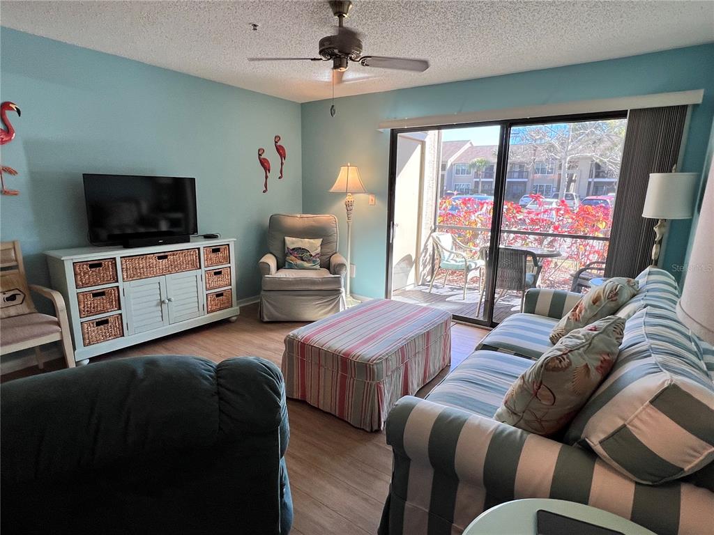 A living room features light blue walls, a striped sofa, a matching ottoman, and sliding doors — 4040 CROCKERS LAKE BOULEVARD UNIT 1717, SARASOTA, FL