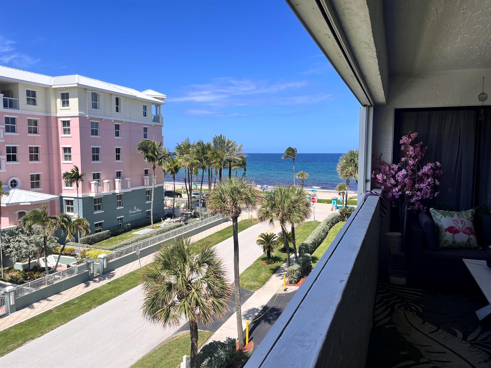 A balcony view overlooks a street, palm trees, a pink building, and the ocean — 330 SE 20th Avenue # 416, Deerfield Beach FL 33441, DEERFIELD BEACH, FL