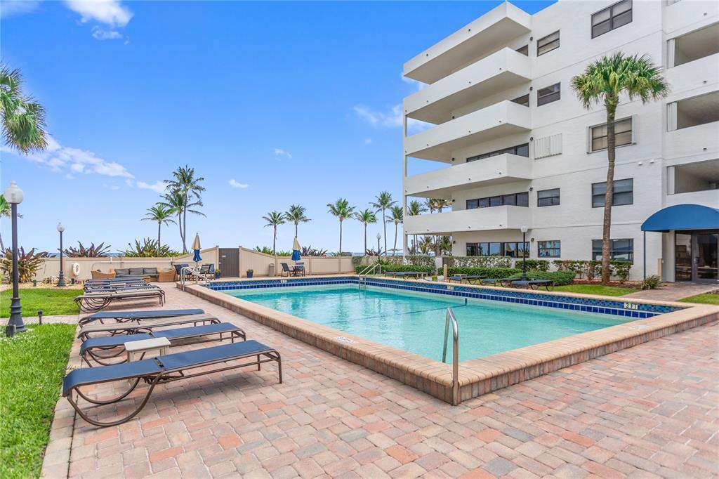A rectangular swimming pool sits on a brick patio next to a multi-story apartment building — 330 SE 20th Avenue # 416, Deerfield Beach FL 33441, DEERFIELD BEACH, FL