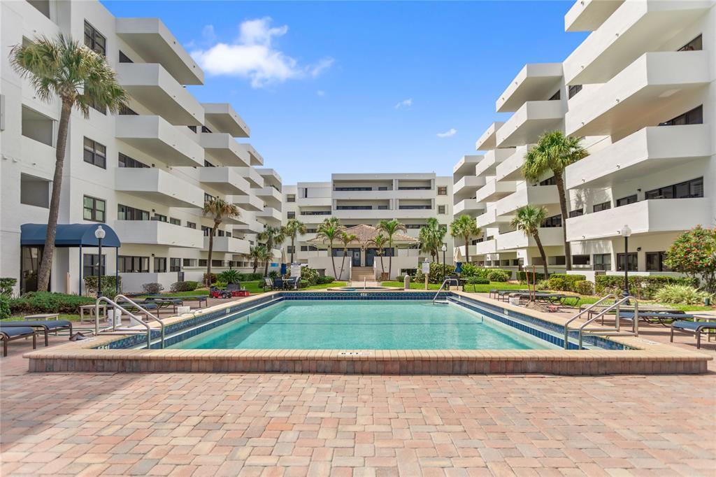 An outdoor swimming pool is situated between two white multi-story apartment buildings with balconies — 330 SE 20th Avenue # 416, Deerfield Beach FL 33441, DEERFIELD BEACH, FL