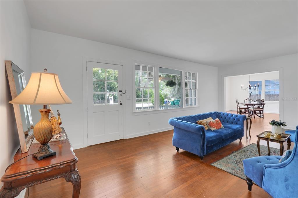 A living room with hardwood floors, a blue tufted sofa, and a white front door — 504 E CITRUS AVE, EUSTIS, FL