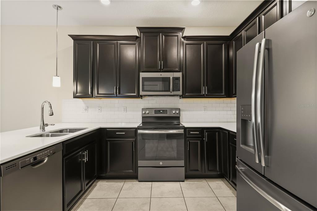 A kitchen features dark wood cabinets, stainless steel appliances, white countertops, and a subway tile backsplash — 4642 TRIBUTE TRAIL, KISSIMMEE, FL