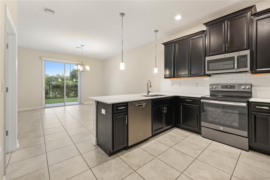 A kitchen with dark cabinets, stainless steel appliances, and an island overlooking a dining area — 4642 TRIBUTE TRAIL, KISSIMMEE, FL