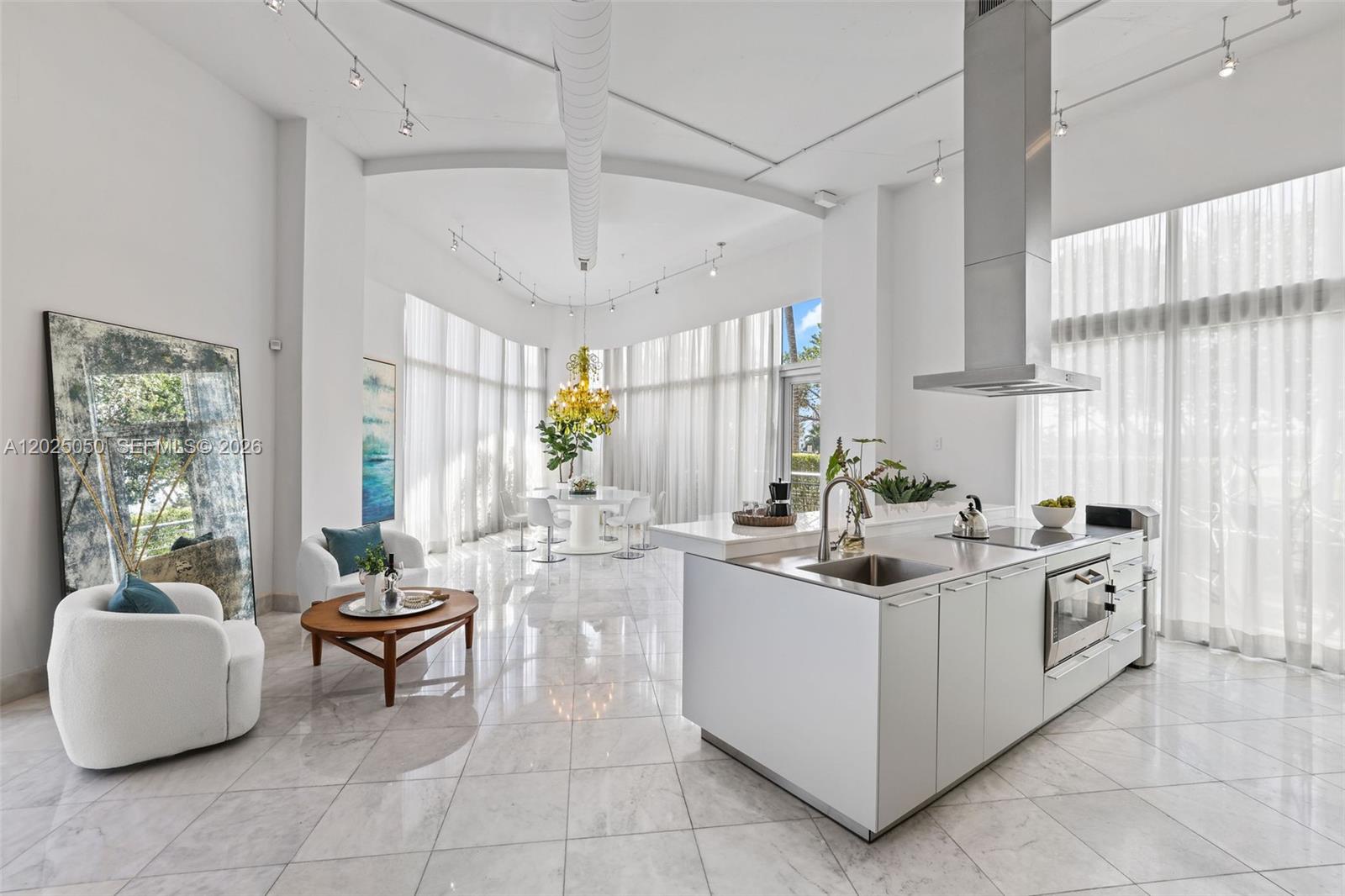 A modern, open-concept kitchen and living area features white cabinetry, marble floors, and floor-to-ceiling curtains — 2001 Meridian Ave # 101, Miami Beach FL 33139, MIAMI BEACH, FL