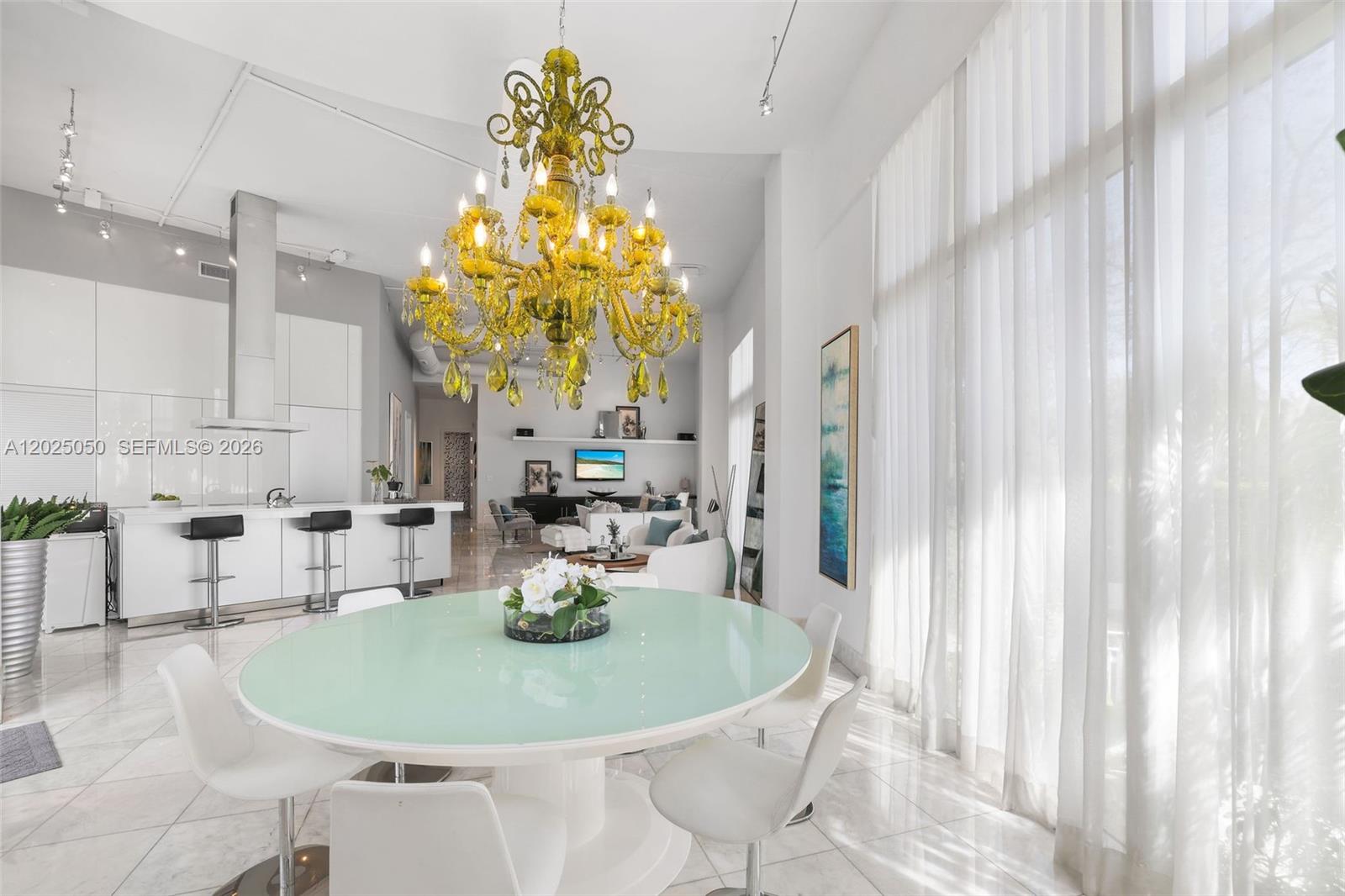 A bright, open-concept dining and kitchen area features a large yellow chandelier and white furniture — 2001 Meridian Ave # 101, Miami Beach FL 33139, MIAMI BEACH, FL