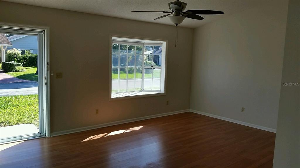 An empty room features wood-look flooring, a ceiling fan, a bay window, and sliding doors — 4 PAR DRIVE, NEW SMYRNA BEACH, FL