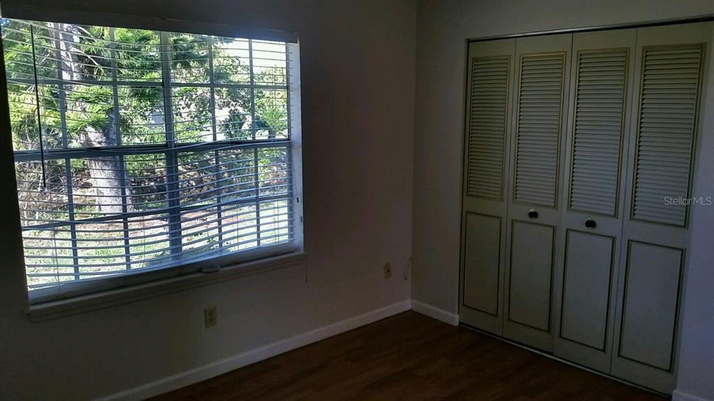 A bedroom features light-colored walls, wood-look flooring, a large window, and bi-fold closet doors — 4 PAR DRIVE, NEW SMYRNA BEACH, FL