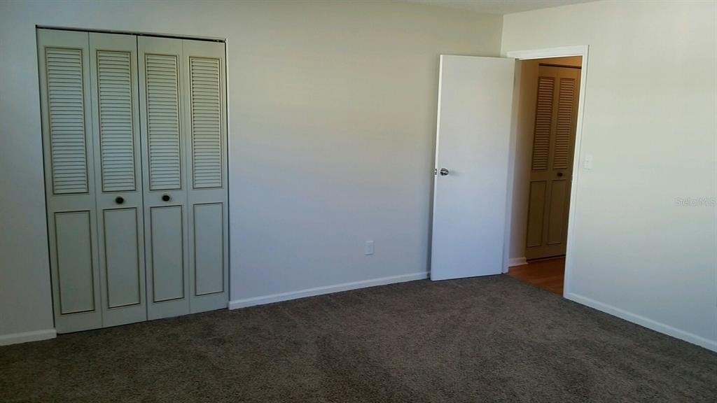 A bedroom features beige carpet, a white door, and a set of louvered closet doors — 4 PAR DRIVE, NEW SMYRNA BEACH, FL
