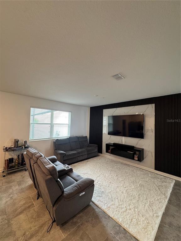 A living room features gray reclining sofas, a white area rug, and a marble-accented media wall — 11924 BOLDFACE DRIVE, ORLANDO, FL