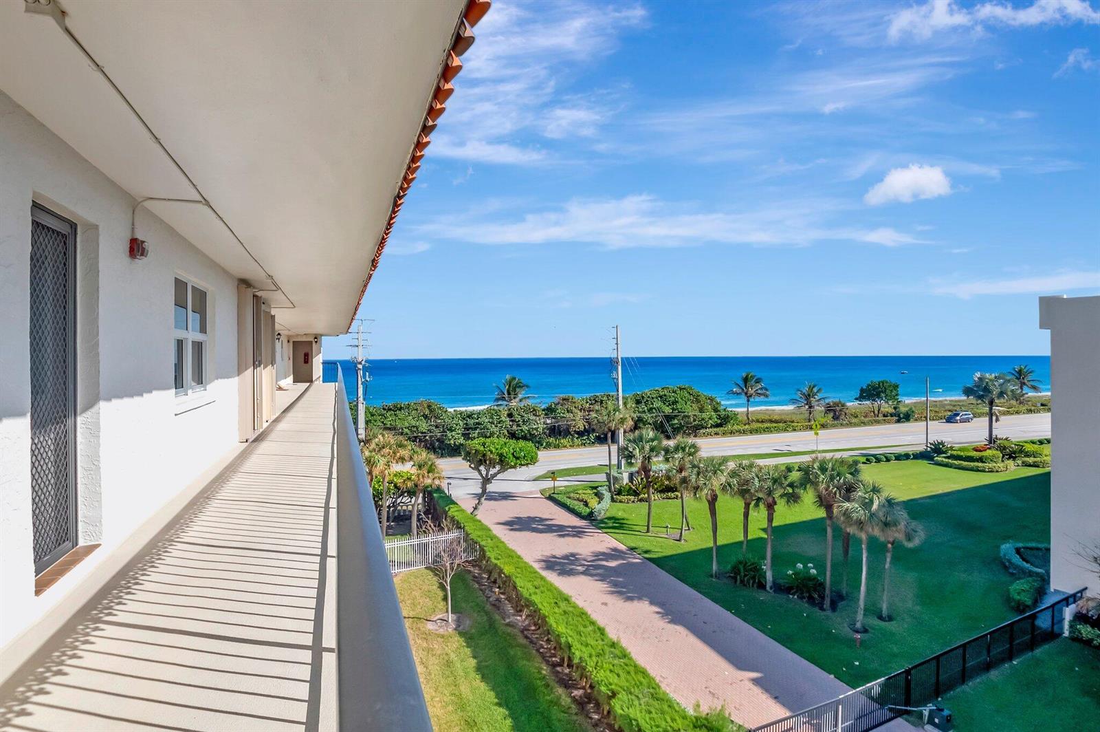 An elevated view from a balcony overlooking a coastal road, palm trees, and the ocean — 2871 N Ocean Boulevard # D506, Boca Raton FL 33431, BOCA RATON, FL