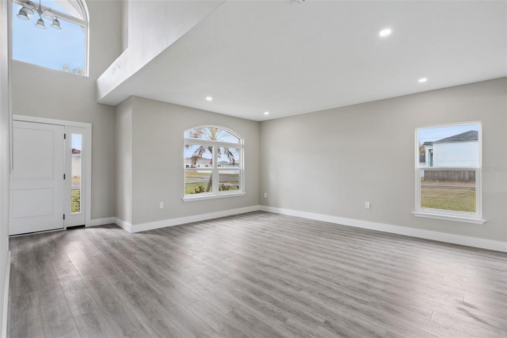 An empty living room with light gray walls, wood-look flooring, and a high vaulted ceiling — 2291 RIO GRANDE CANYON LOOP, KISSIMMEE, FL