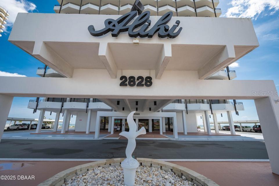 The exterior entrance of a multi-story building features a large white sign reading Aliki — 2828 N ATLANTIC AVENUE UNIT 302, DAYTONA BEACH, FL