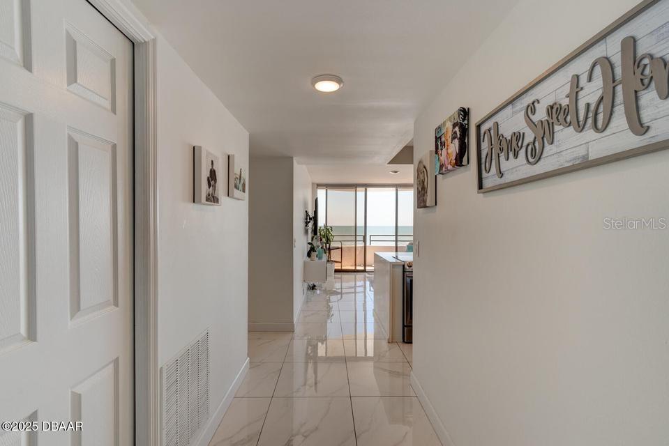 A hallway with white walls and tiled floors leads toward a balcony overlooking the ocean — 2828 N ATLANTIC AVENUE UNIT 302, DAYTONA BEACH, FL
