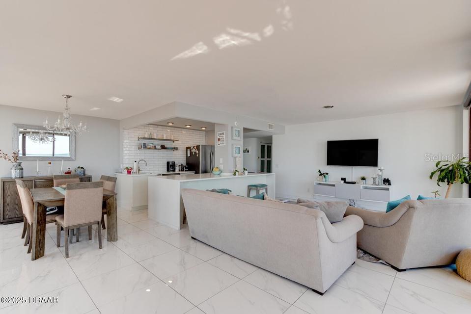 An open-concept living and dining area features white tile floors and a modern kitchen — 2828 N ATLANTIC AVENUE UNIT 302, DAYTONA BEACH, FL