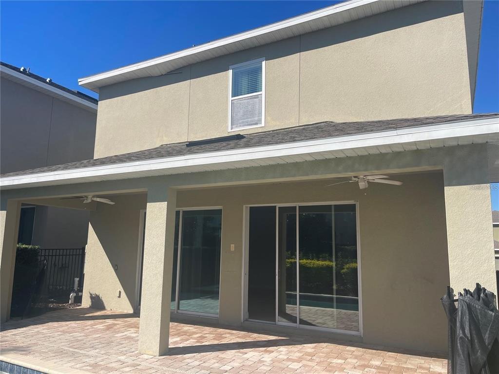 A covered patio with a paver floor and sliding glass doors leads into a house — 210 PENDANT COURT, KISSIMMEE, FL
