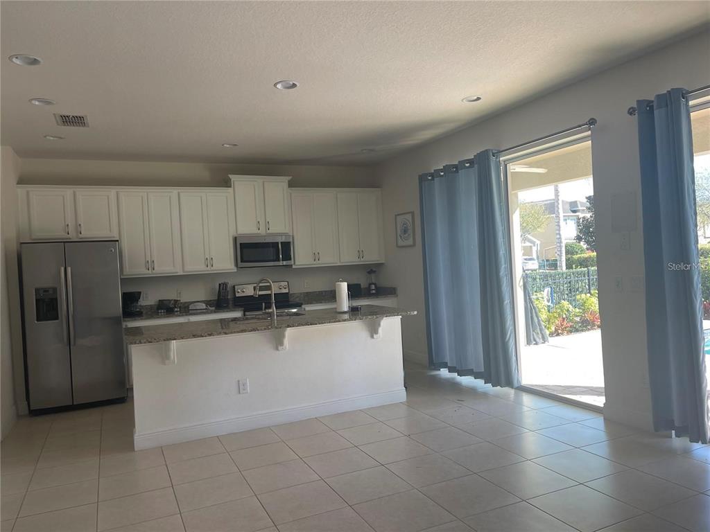 A kitchen with white cabinets, stainless steel appliances, and a granite island overlooks a patio — 210 PENDANT COURT, KISSIMMEE, FL