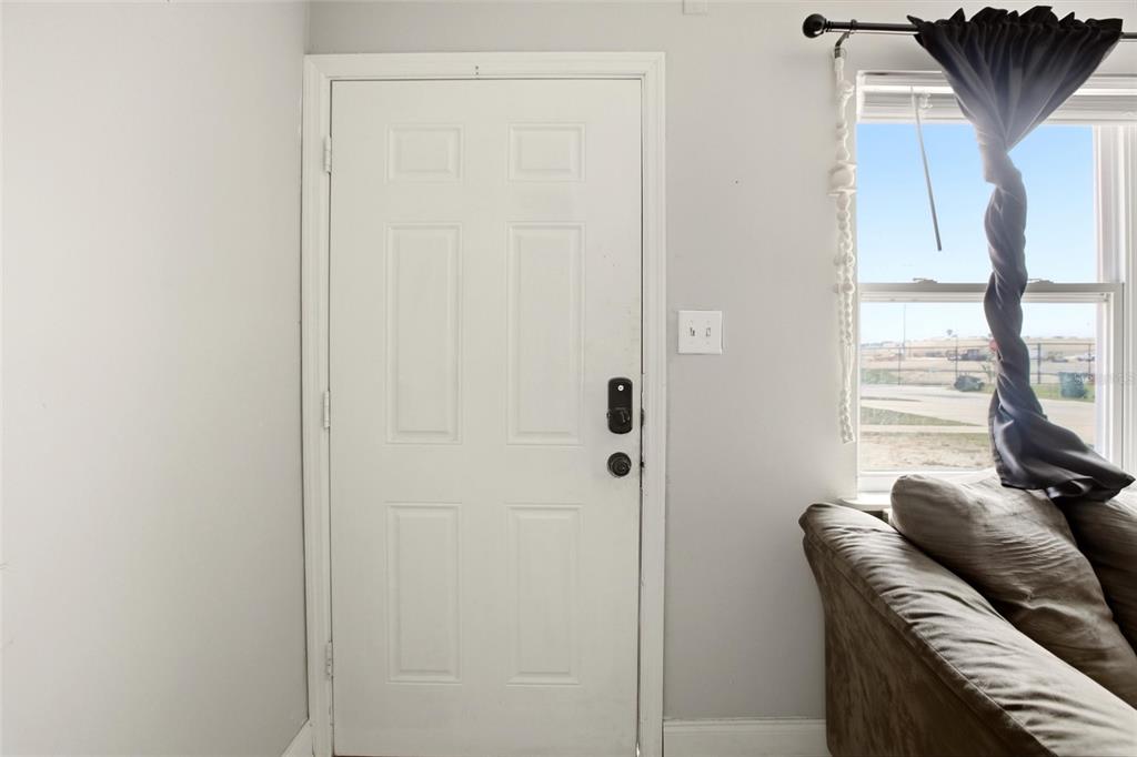 A white door with a black handle sits next to a window with gray curtains — 1702 BIRCHWOOD CIRCLE, LEESBURG, FL