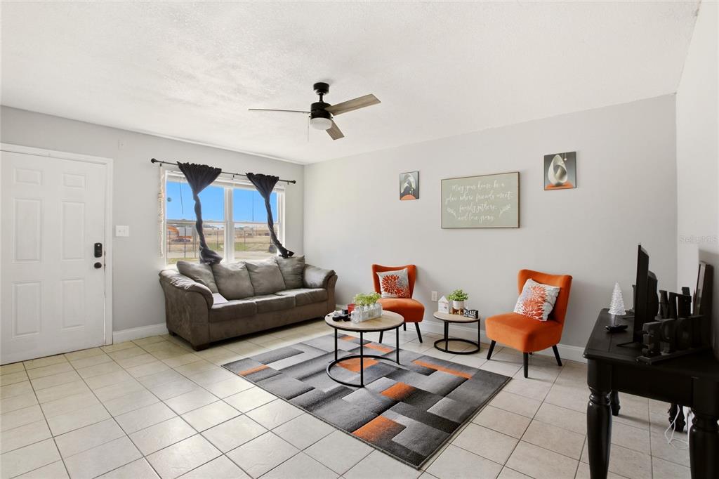 A living room features a gray sofa, two orange chairs, a rug, and tile flooring — 1702 BIRCHWOOD CIRCLE, LEESBURG, FL