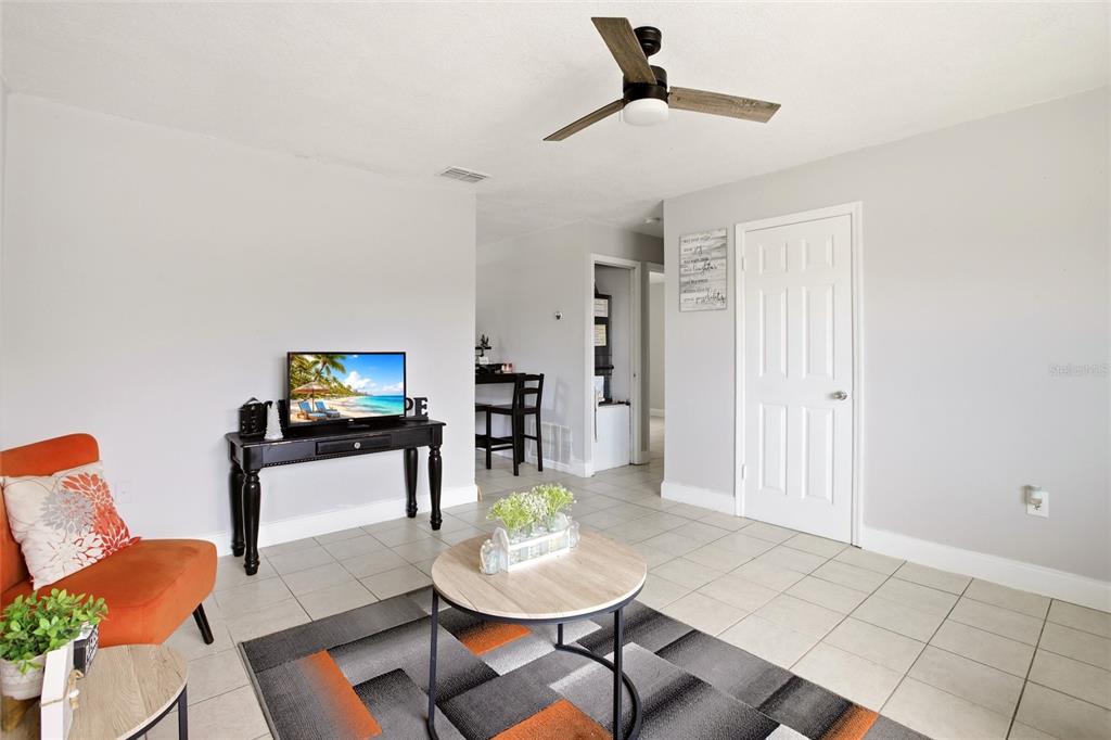 A living room features light gray walls, tile flooring, an orange chair, and a ceiling fan — 1702 BIRCHWOOD CIRCLE, LEESBURG, FL